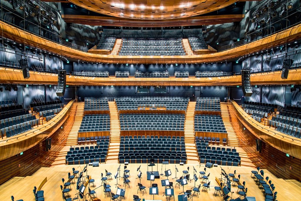 Modern concert hall seen from a high balcony, with tiered seating facing the stage